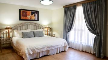 Cama bem arrumada com cabeceira, duas luminárias de apoio e uma janela grande com cortinas.