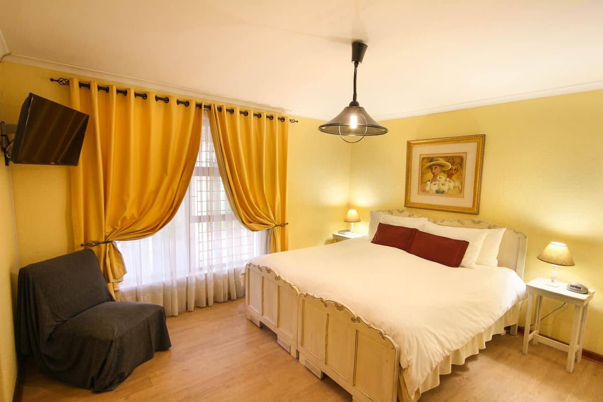 A hotel room with a bed, a chair, a TV, a painting, and two bedside lamps.