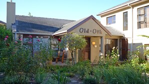 Un bâtiment sur lequel est apposée une enseigne indiquant « Old Osk ». Il est doté d’un jardin où l’on trouve diverses plantes et fleurs, d’un banc et d’un chemin menant à l’entrée.
