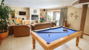 Une table de billard dans un salon, avec un canapé et des fauteuils, un téléviseur et un coin repas comprenant une table et des chaises.