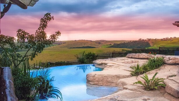 A swimming pool with a view of rolling hills and a sunset sky. - Rain Farm Game Lodge (Ballito)
