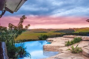 A swimming pool with a view of rolling hills and a sunset sky. - Rain Farm Game Lodge (Ballito)