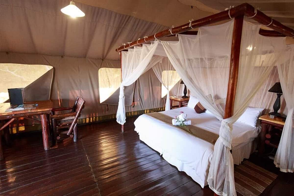 A tented room with a four-poster bed, a wooden desk, and a chair.