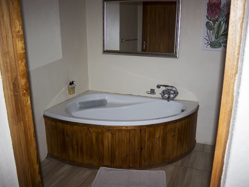 A wooden bathtub in a bathroom with a wooden door frame, a mirror, and a small towel on the floor.