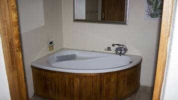A wooden bathtub in a bathroom with a wooden door frame, a mirror, and a small towel on the floor.