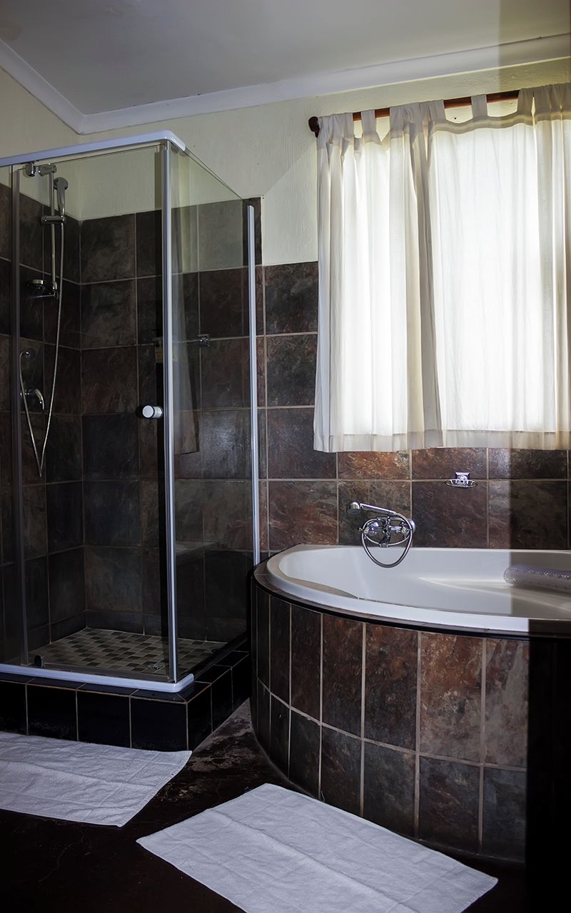 A bathroom with a glass-enclosed shower, a freestanding bathtub, and a window with curtains.