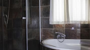 A bathroom with a glass-enclosed shower, a freestanding bathtub, and a window with curtains.