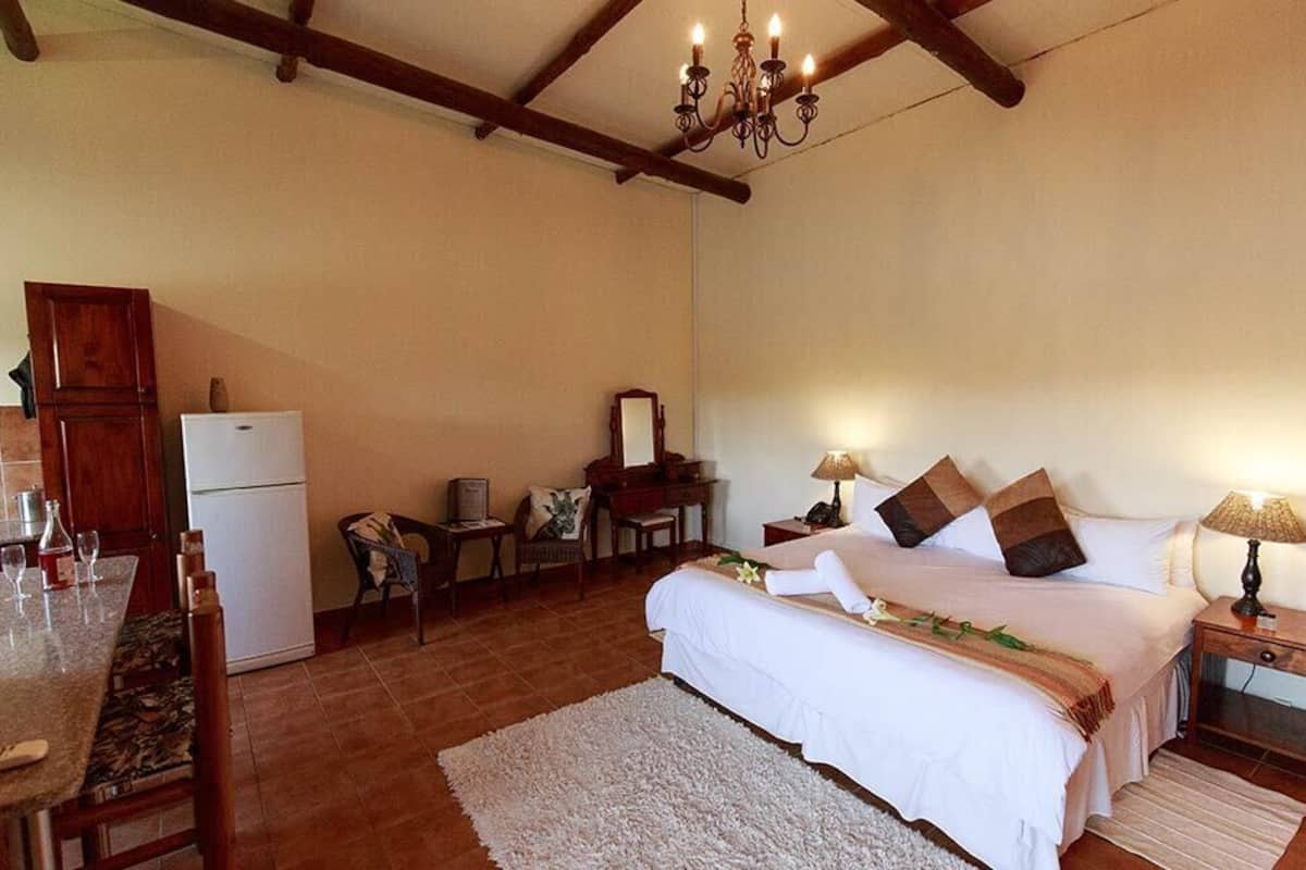 A bedroom with a bed, bedside tables, a desk, a chair, a refrigerator, and a chandelier.