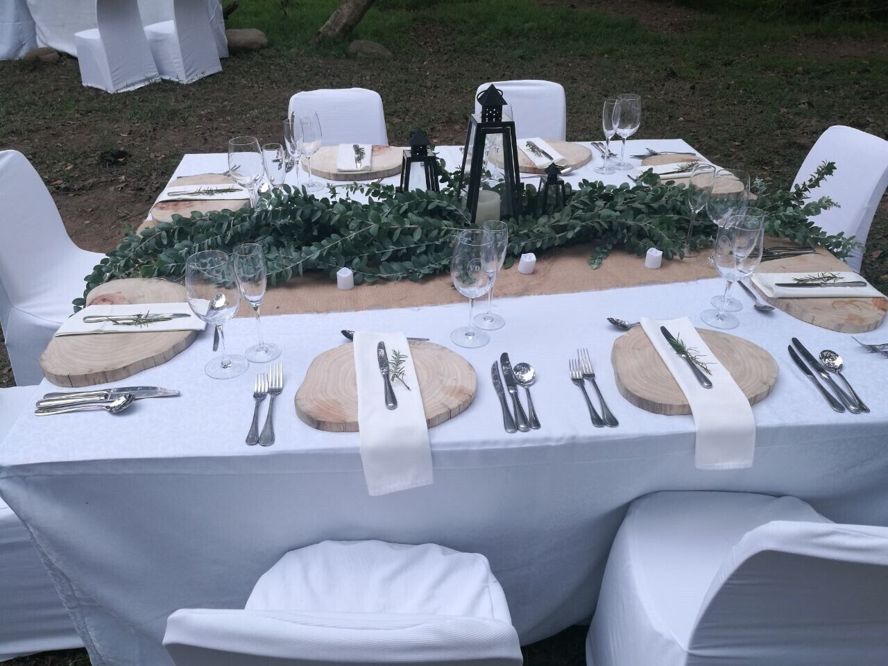 Una mesa preparada para una comida, con manteles blancos, tablas de madera para servir y cubiertos.