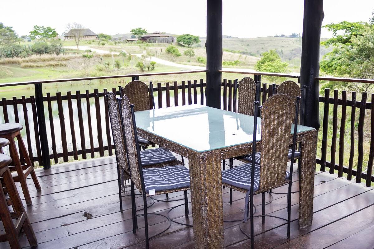 A covered outdoor dining area with a glass table and wicker chairs, overlooking a scenic landscape.