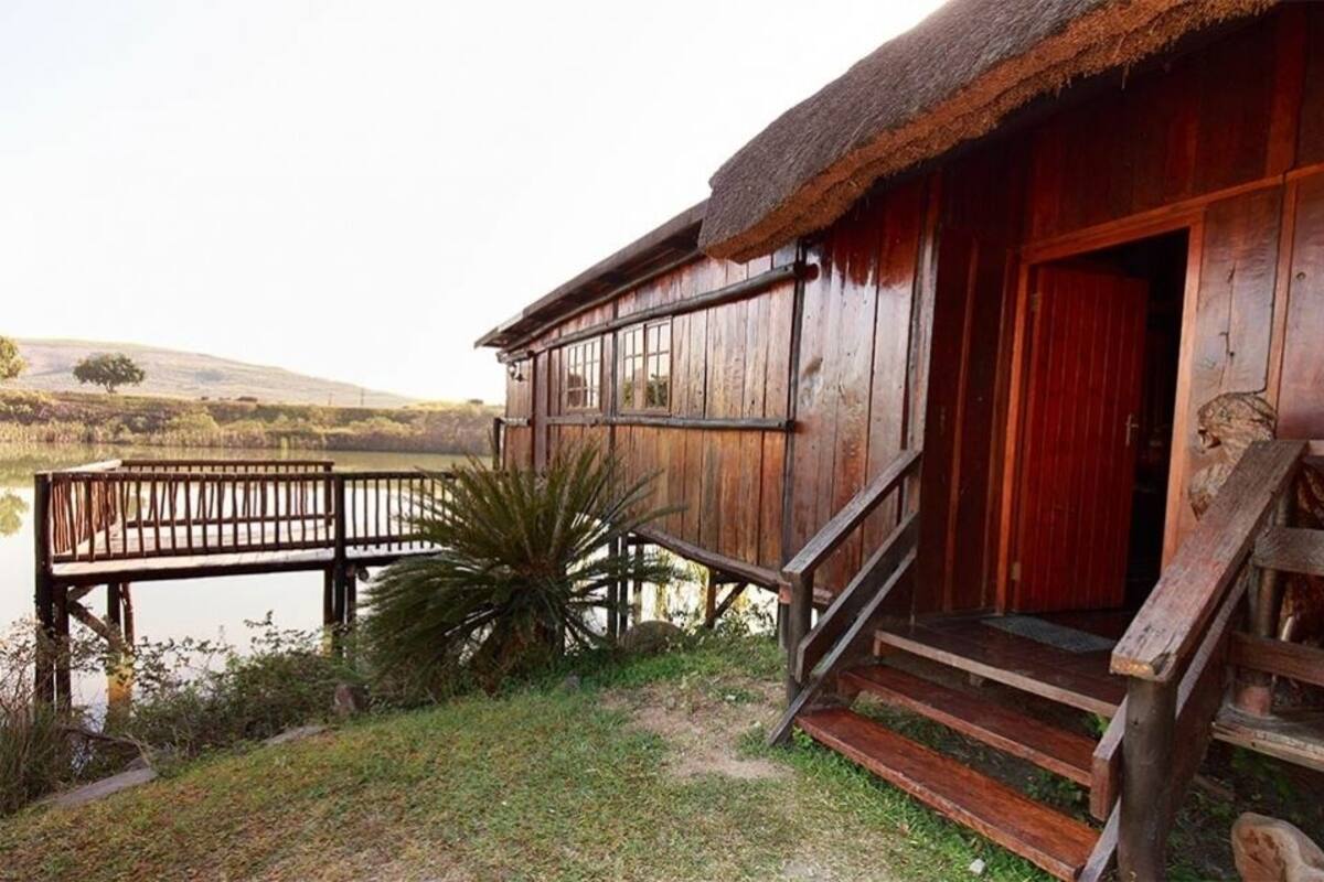 A wooden cabin with a thatched roof, a wooden deck, and a view of a lake.