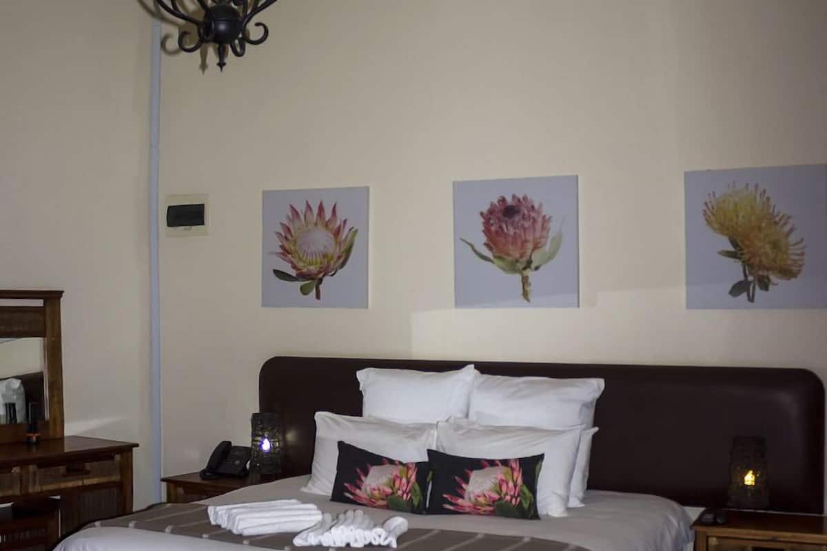 A bedroom with a large bed, a chandelier, and three floral paintings on the wall.