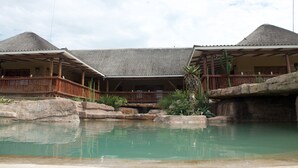 A resort with a pool, wooden structures, and a thatched roof. - Rain Farm Game Lodge (Ballito)