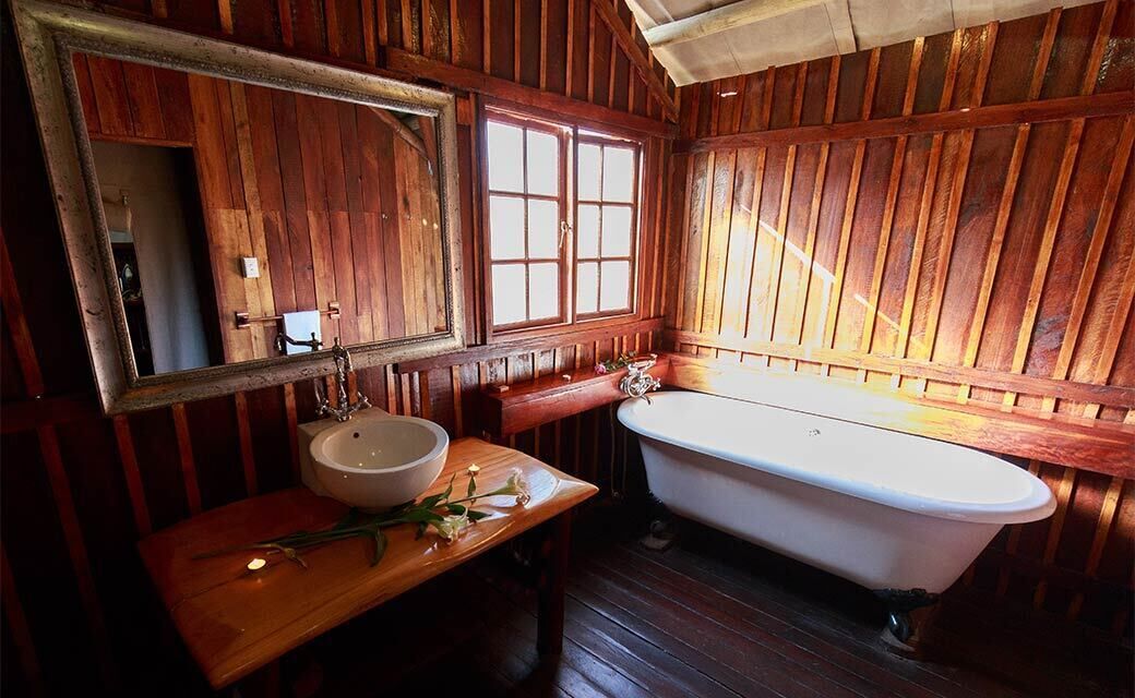 A wooden cabin bathroom with a wooden vanity, a white sink, a mirror, and a white bathtub.