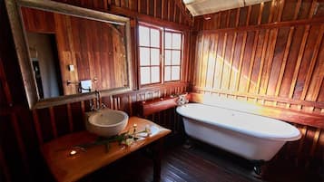 A wooden cabin bathroom with a wooden vanity, a white sink, a mirror, and a white bathtub.