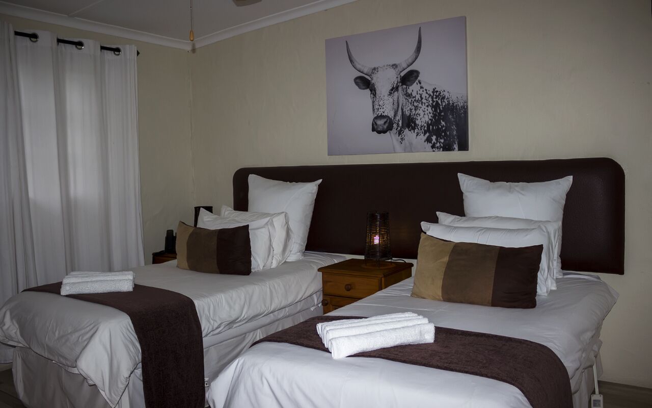 Quarto de hotel com duas camas, cabeceira, mesa de cabeceira e uma pintura de um touro na parede.