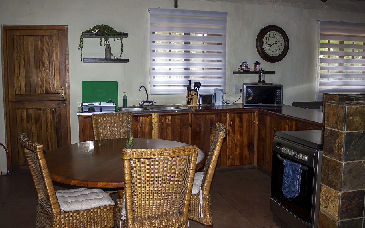 A kitchen with a dining table, chairs, a microwave, a stove, and a clock on the wall.