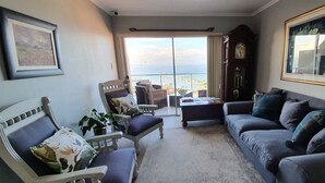 A living room with a view of the sea, a large clock, and a framed picture on the wall. - 3 Colours Blue (Mossel Bay)
