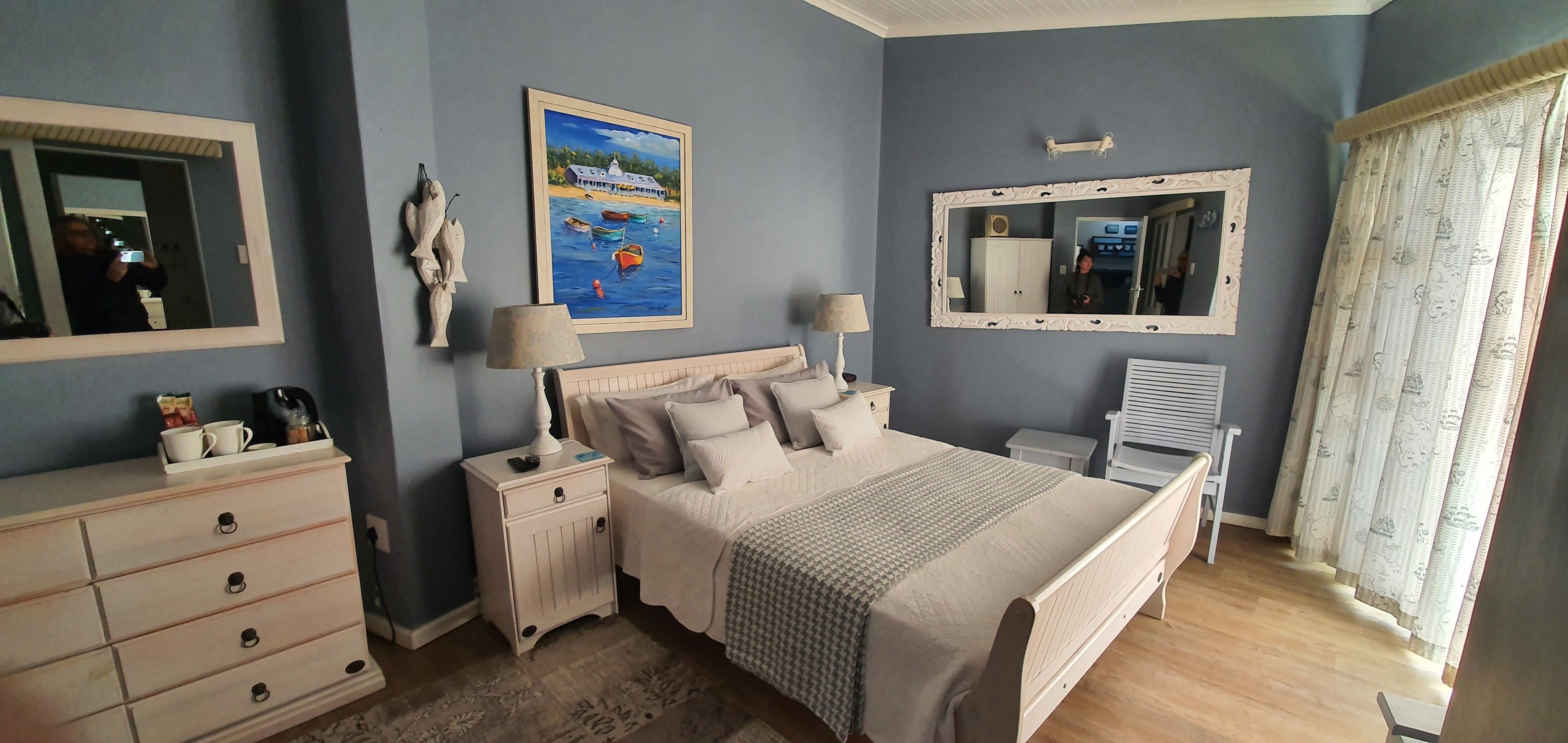 A bedroom with a bed, bedside tables, a dresser, a painting, and a mirror.