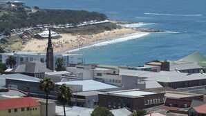 A coastal town with a beach, buildings, and a church steeple. - 3 Colours Blue (Mossel Bay)