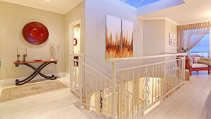 Un amplio salón con techo alto, una escalera con barandilla blanca y un gran ventanal con vistas a un balcón.