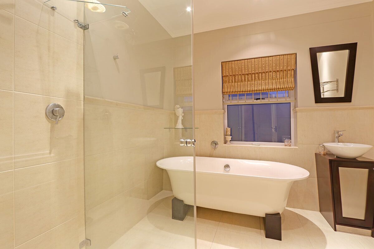 A modern bathroom with a freestanding bathtub, a glass shower enclosure, a vanity with a sink, and a window with a patterned curtain.