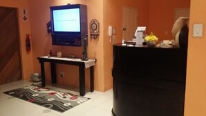 Een woonkamer met een televisie, een zwarte bank, een kleintje tafeltje met een bloevas en een kamerkleed met dessin.