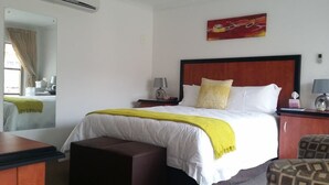 Een hotelkamer met een bed, nachtkastje, stoel, bureau, airconditioning en een raam met gordijnen.