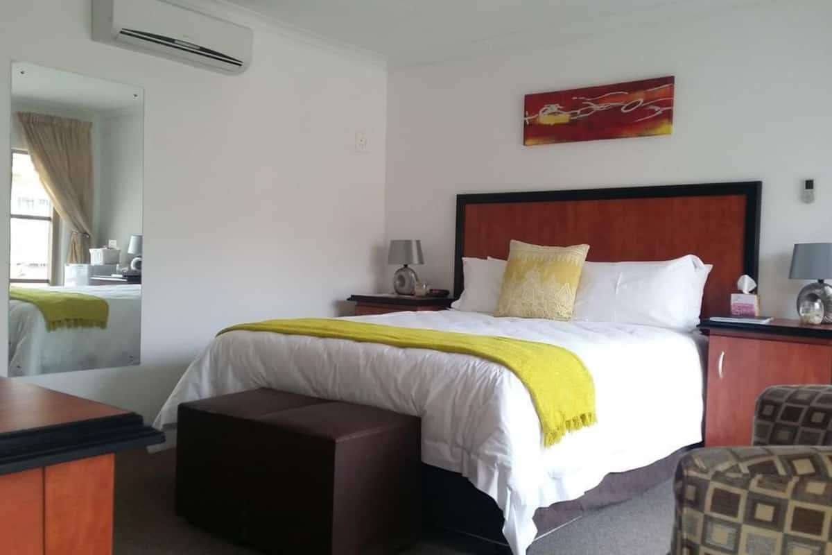 Habitación de hotel con cama, mesita de noche, silla, escritorio, aire acondicionado y ventana con cortinas.