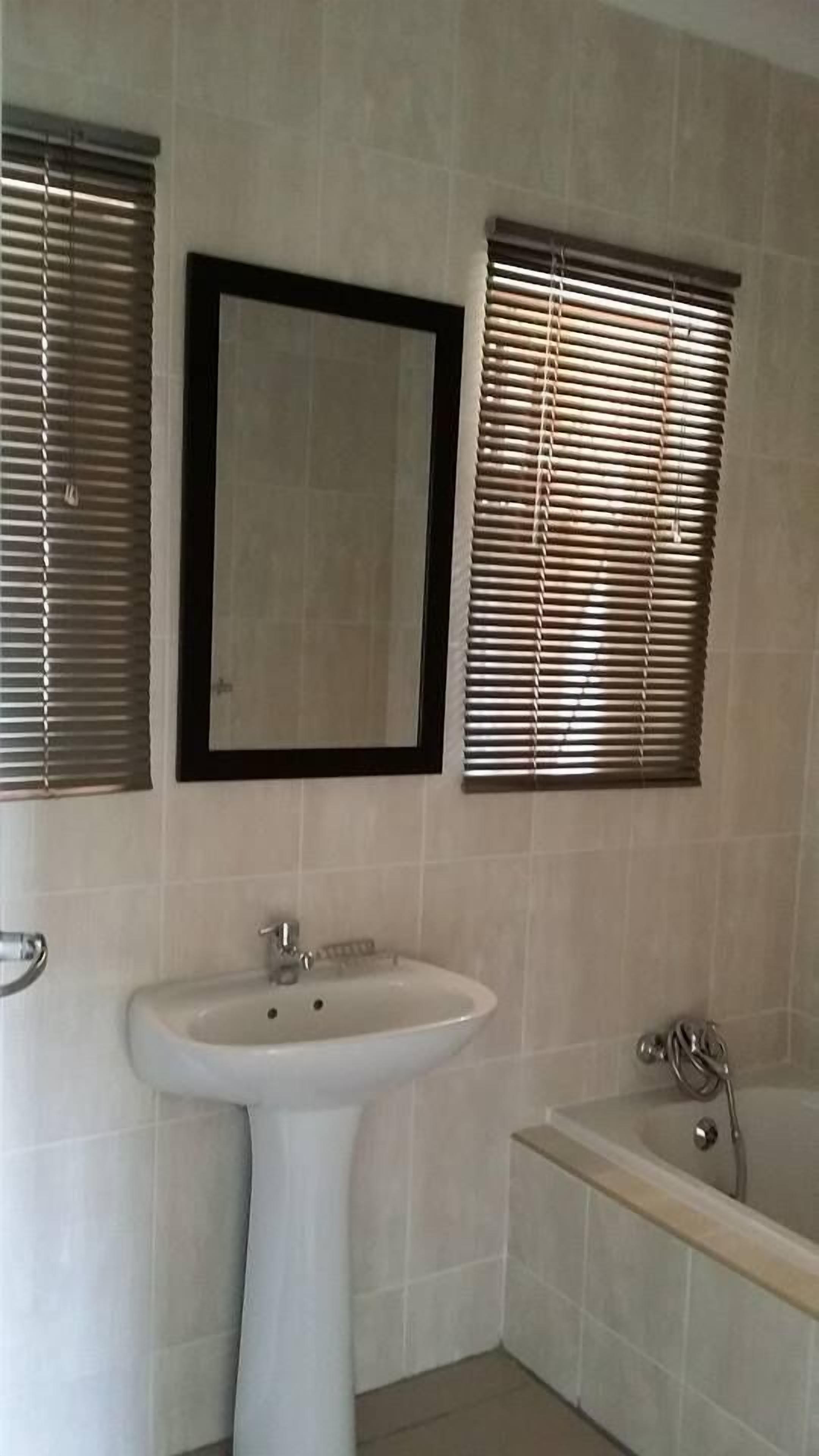 A bathroom with a pedestal sink, a bathtub, and two windows with blinds.
