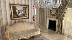 A luxurious living room with a classic sofa, a chandelier, a fireplace, and a framed painting on the wall. - Bella Casa Guesthouse (Sandton)