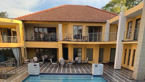 A swimming pool with a wooden deck in front, surrounded by a building with balconies and outdoor seating. - Bella Casa Guesthouse (Sandton)