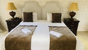 A double bed with a white and brown bedspread, two brown pillows, and two bedside tables with lamps. - Bella Casa Guesthouse (Sandton)