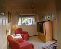 Una habitación con un sillón rojo, un aparador de madera, una mesa con lámpara y una ventana con cortinas.