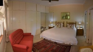 Una camera da letto con un letto grande, una poltrona rossa, un ventilatore a soffitto e un comodino con una lampada.