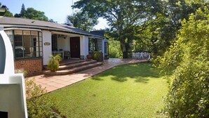 Una casa con un cortile lastricato, un portico con sedie e un albero grande.
