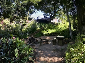 Un jardín con terraza de madera, mesas de picnic y una escalera que lleva a un edificio.