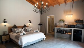 Ein modernes Schlafzimmer mit einem großen Bett, Nachttischlampen und einem Kronleuchter. Angrenzend befindet sich eine kleine Küchenzeile mit Mikrowelle, Toaster und Kaffeemaschine.