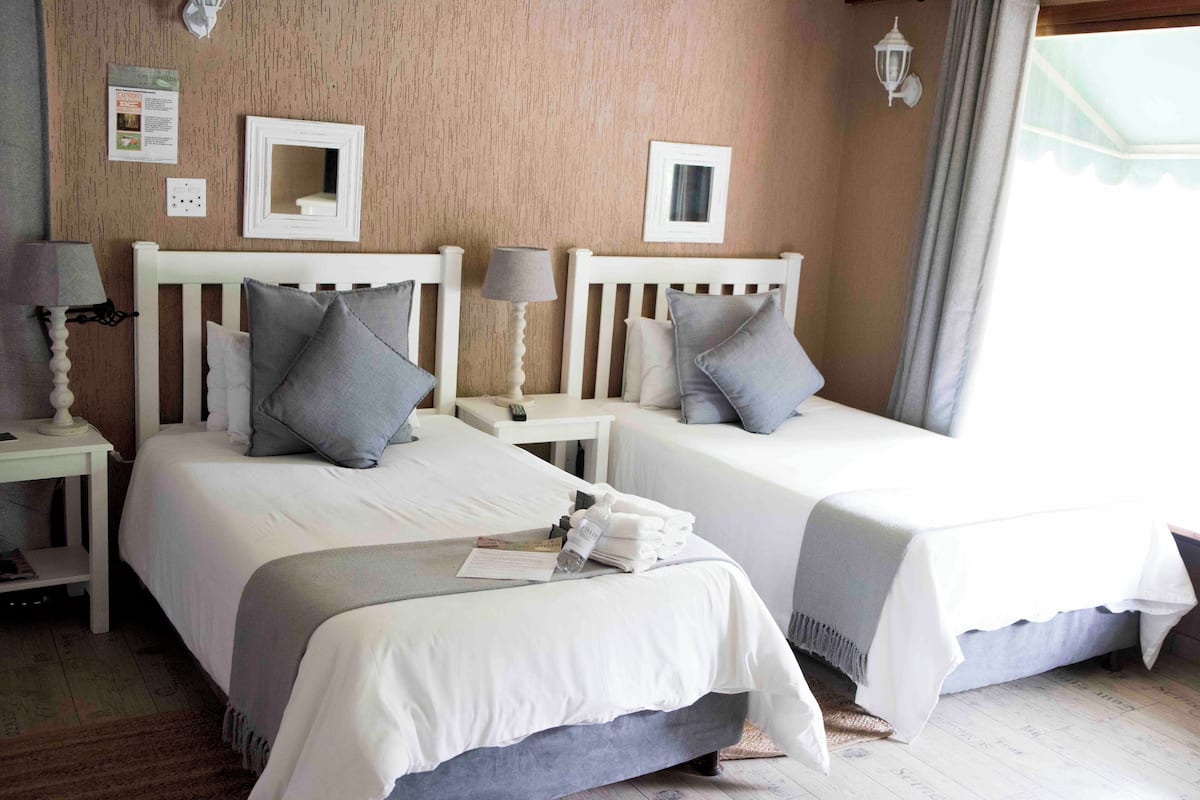 A hotel room with two single beds, white bedding, and a small table with a lamp.