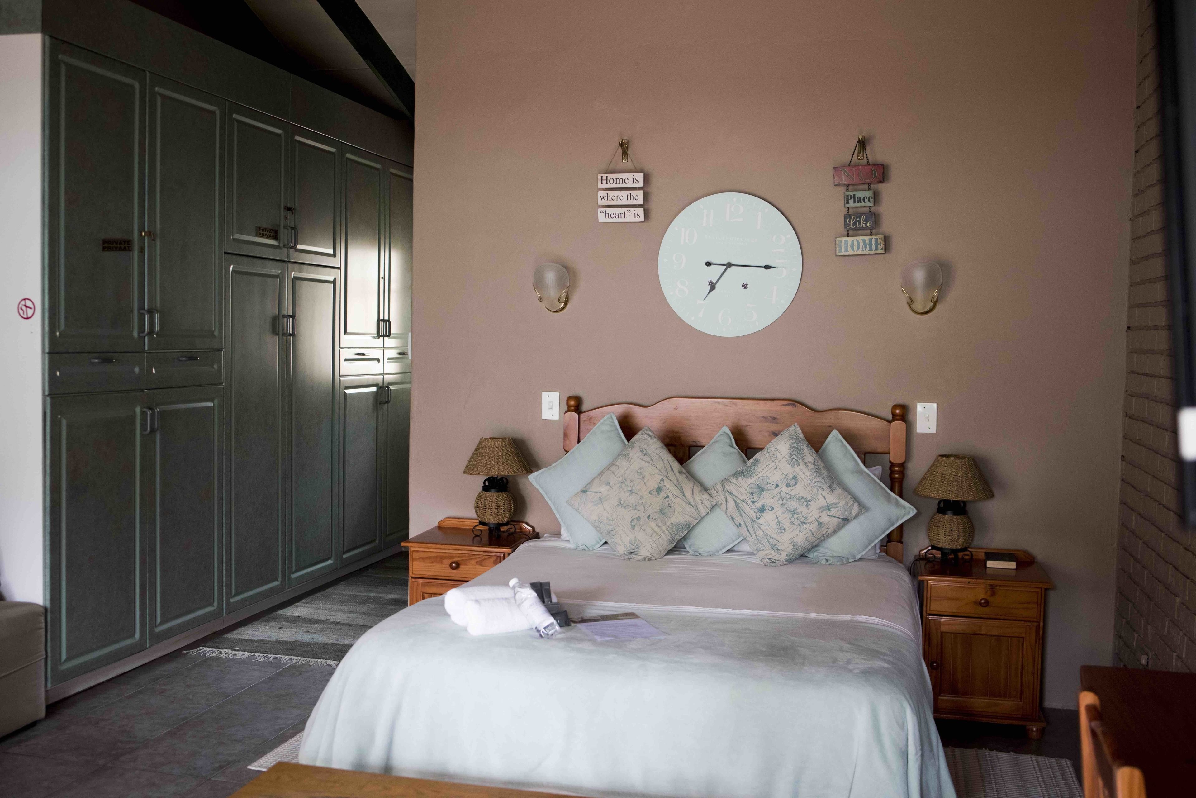 A bedroom with a bed, two bedside tables with lamps, a clock, and a wardrobe.