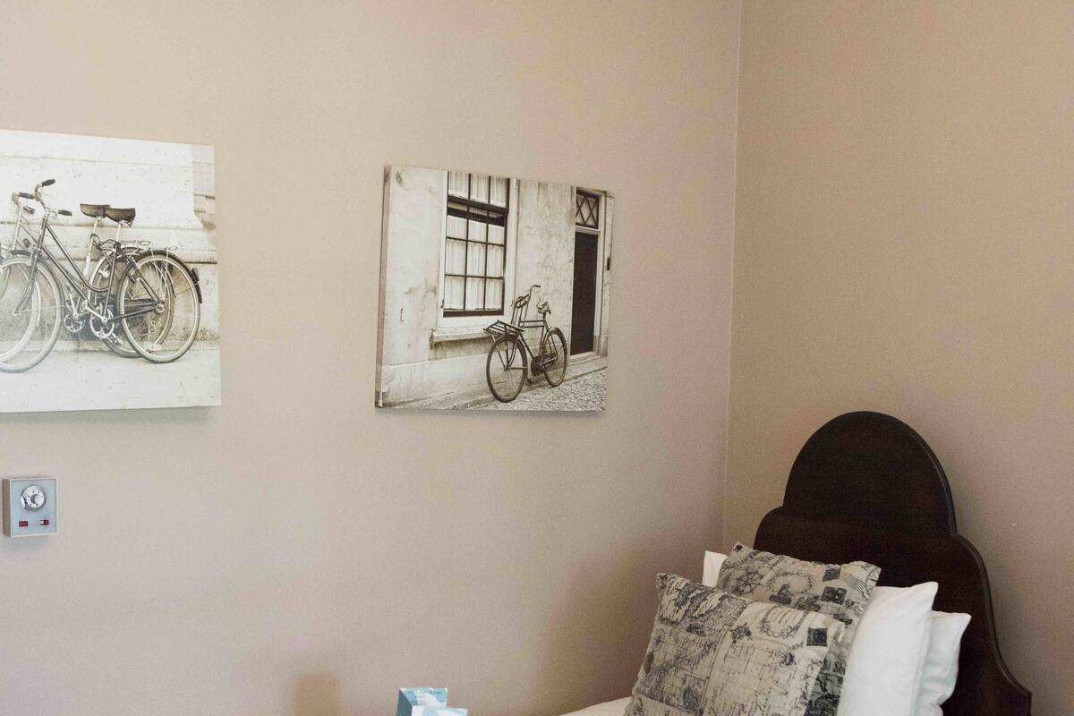 A neatly made bed with a red blanket, a chandelier, and wall art depicting bicycles.