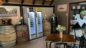 Un interior de restaurante con una mesa y sillas de madera, barriles de vino y un techo de paja.