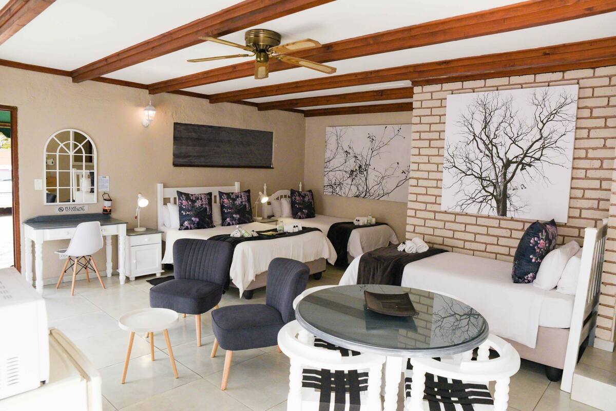 A hotel room with a bed, two chairs, a small table, a desk, and a ceiling fan.