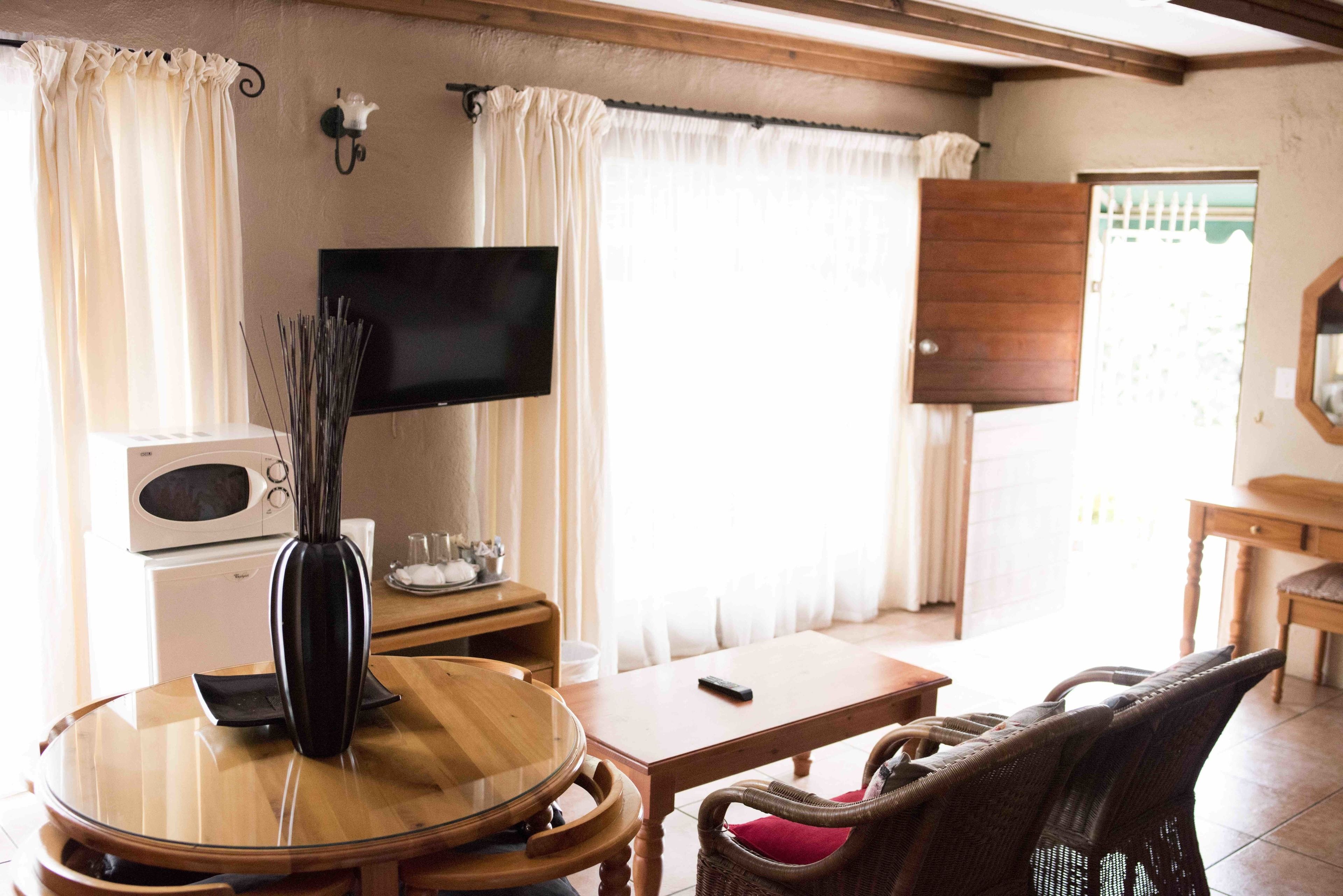 A cozy room with a round wooden table, a wicker chair, a flat-screen TV, a microwave, and a cabinet.