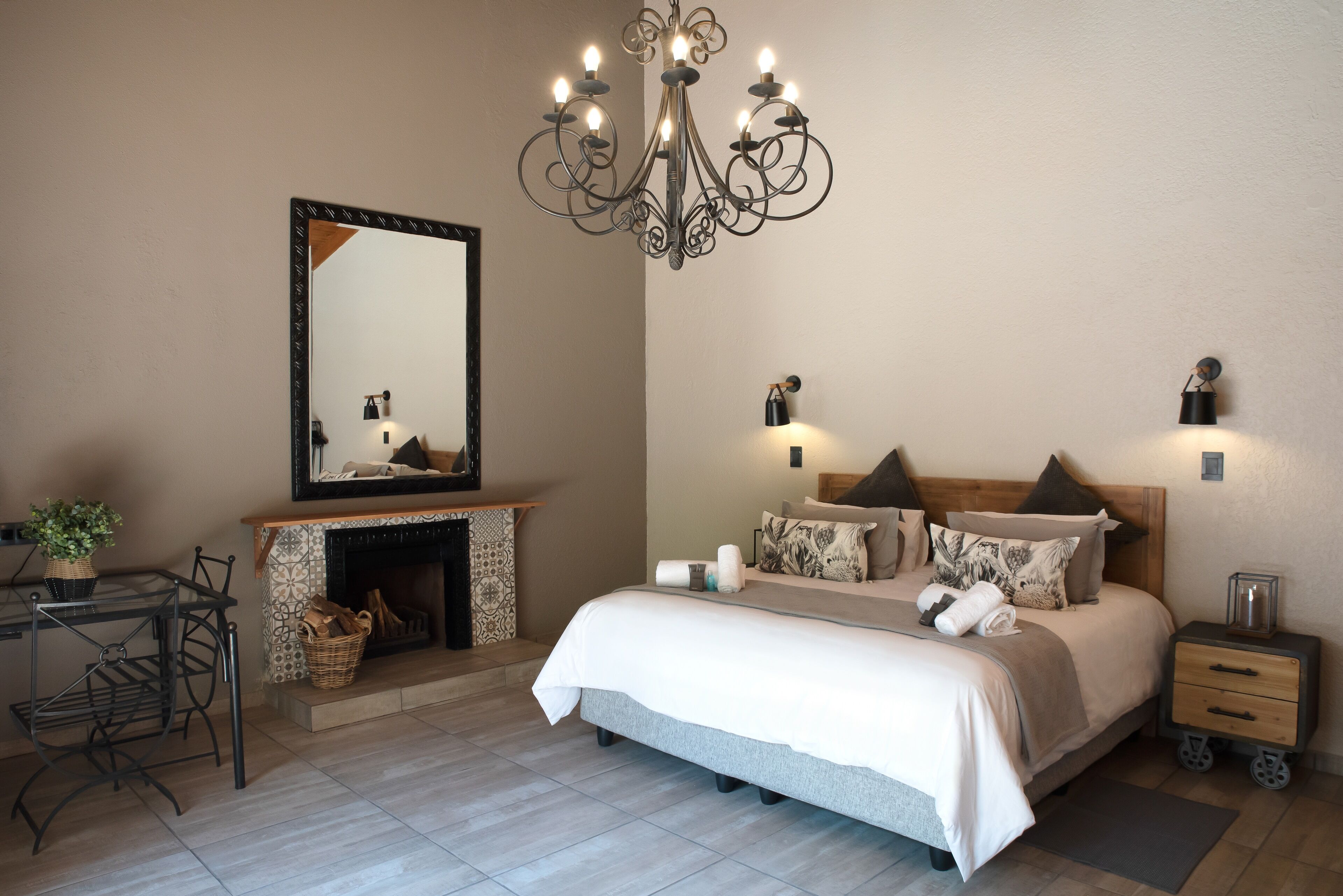 A bedroom with a bed, bedside tables, a mirror, a chandelier, and a fireplace.