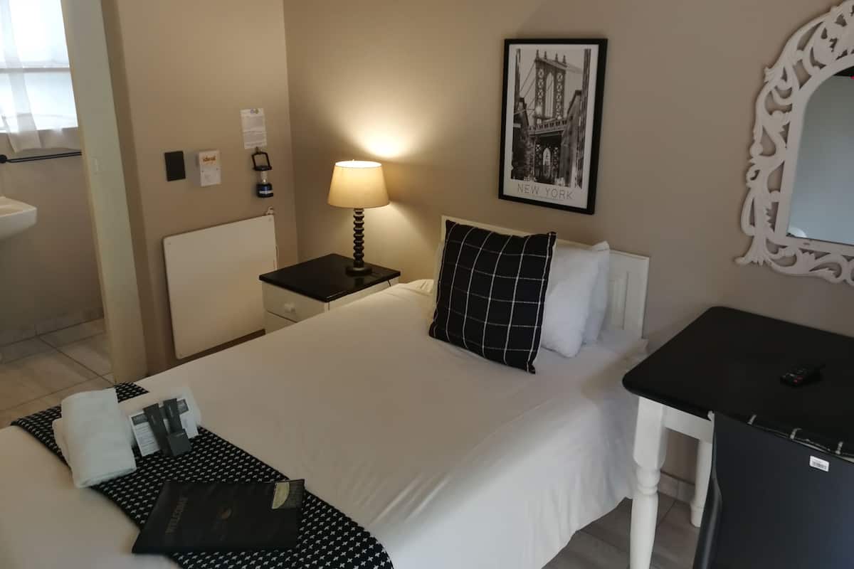 A hotel room with a bed, bedside table, lamp, and a framed picture on the wall.