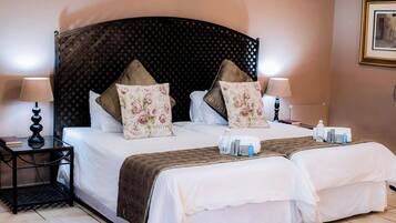 Una cama doble con cabecera oscura, dos mesitas de noche con lámparas y almohadas estampadas con motivos florales.
