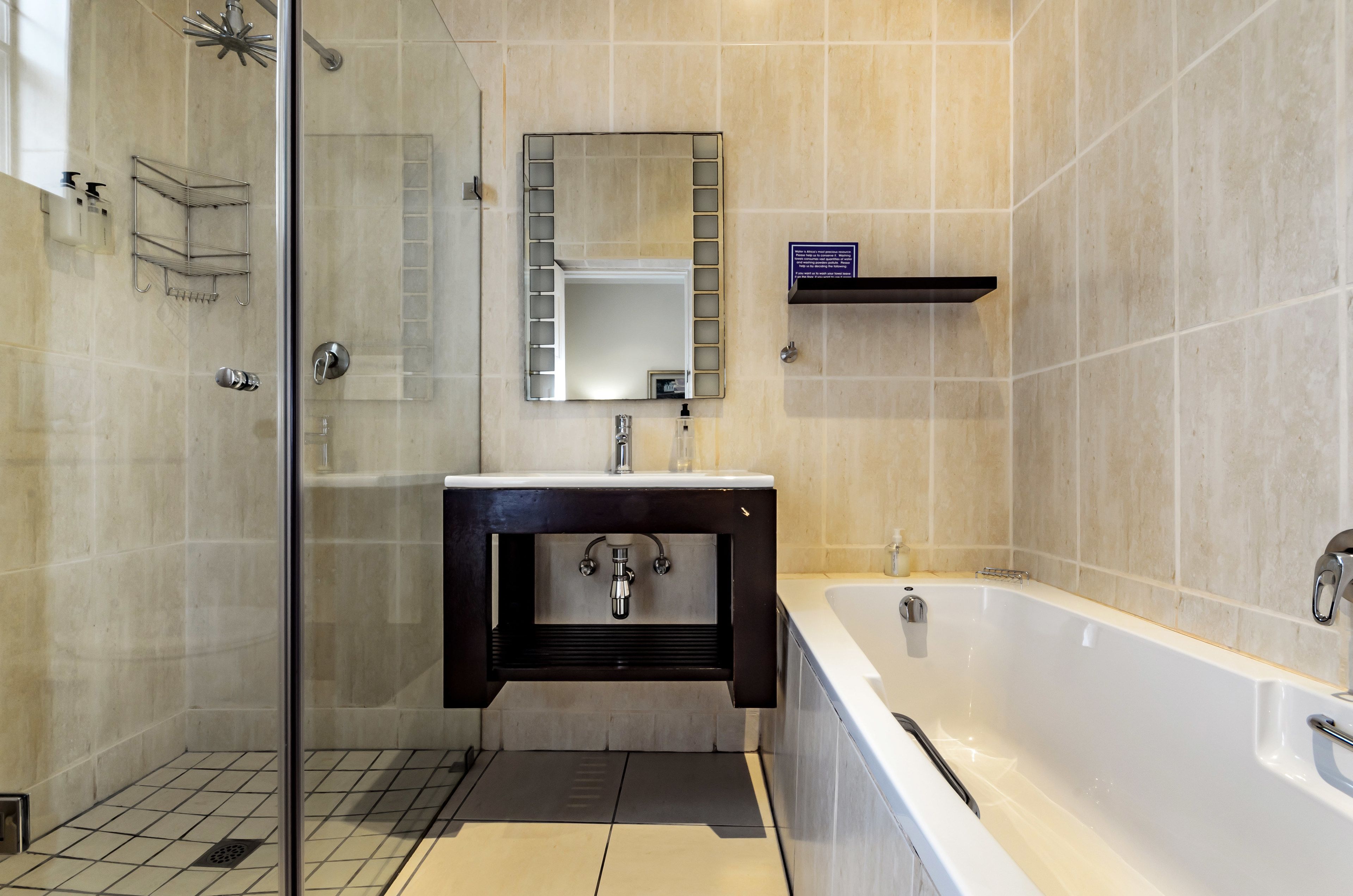 A modern bathroom with a glass-enclosed shower, a large mirror, a white bathtub, and a dark wooden vanity.