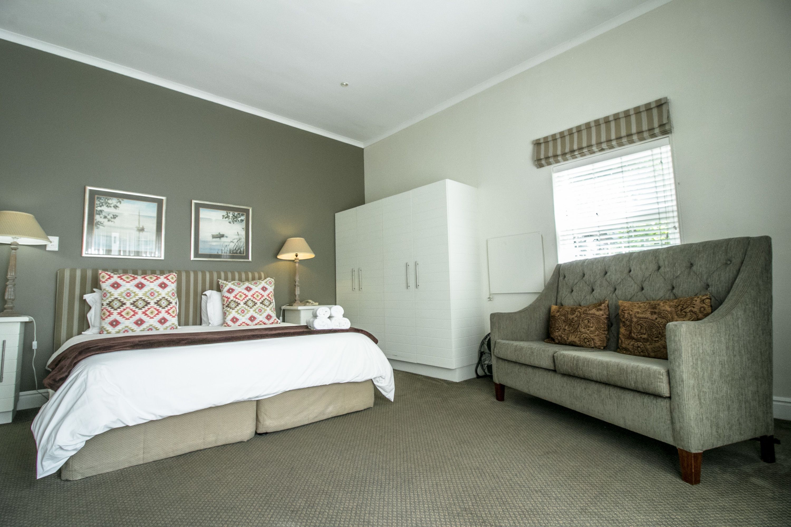 A bedroom with a bed, a grey sofa, a wardrobe, and two wall-mounted lamps.