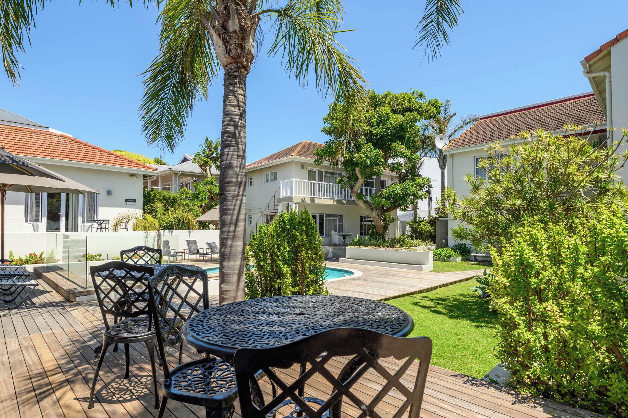 A poolside area with outdoor furniture, a palm tree, and a view of neighboring houses.